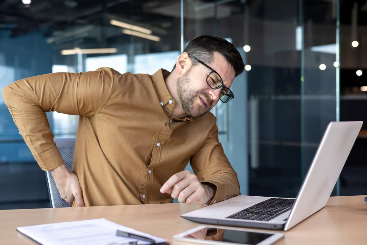 Office worker at a laptop holding their lower back in discomfort