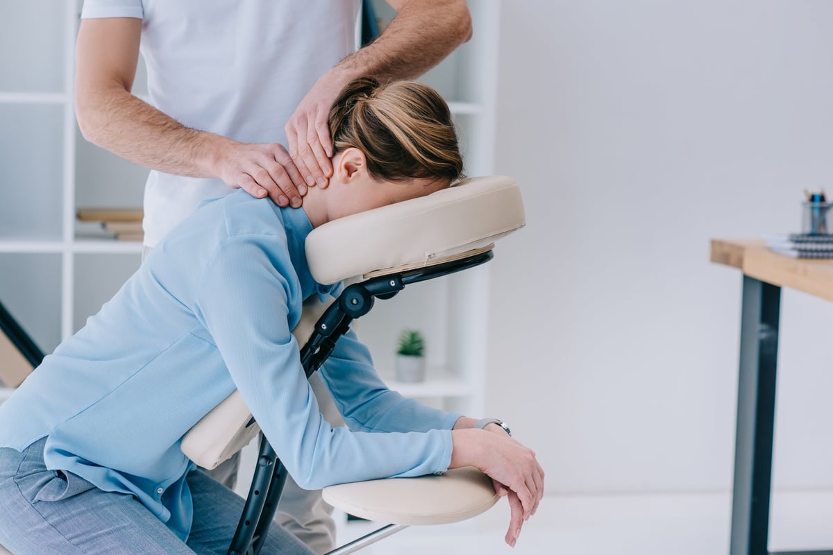 Licensed therapist giving a seated neck and shoulder massage to a businesswoman in her office